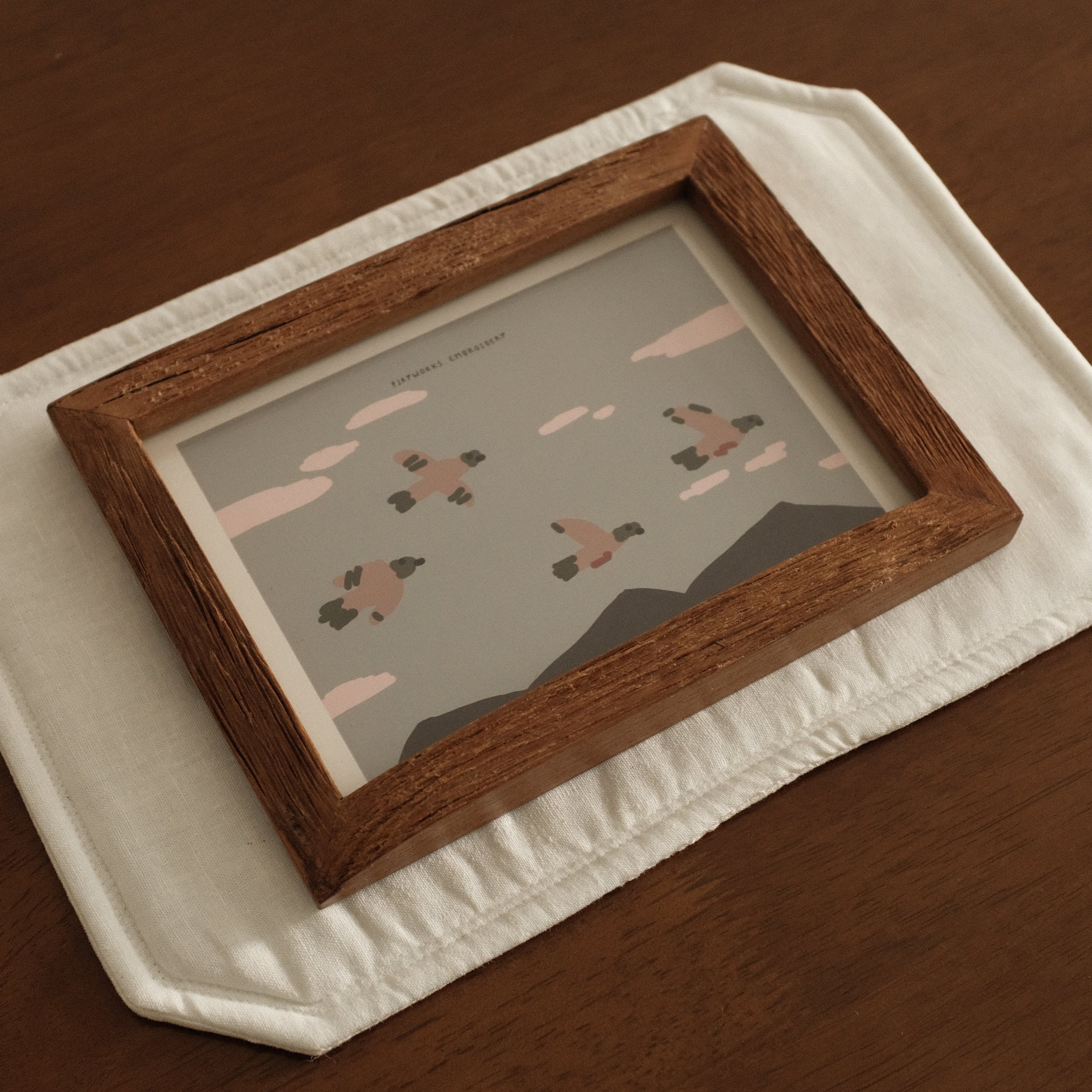 Teak Wooden picture frame with a small painting on a white decorative placemat on a wooden surface