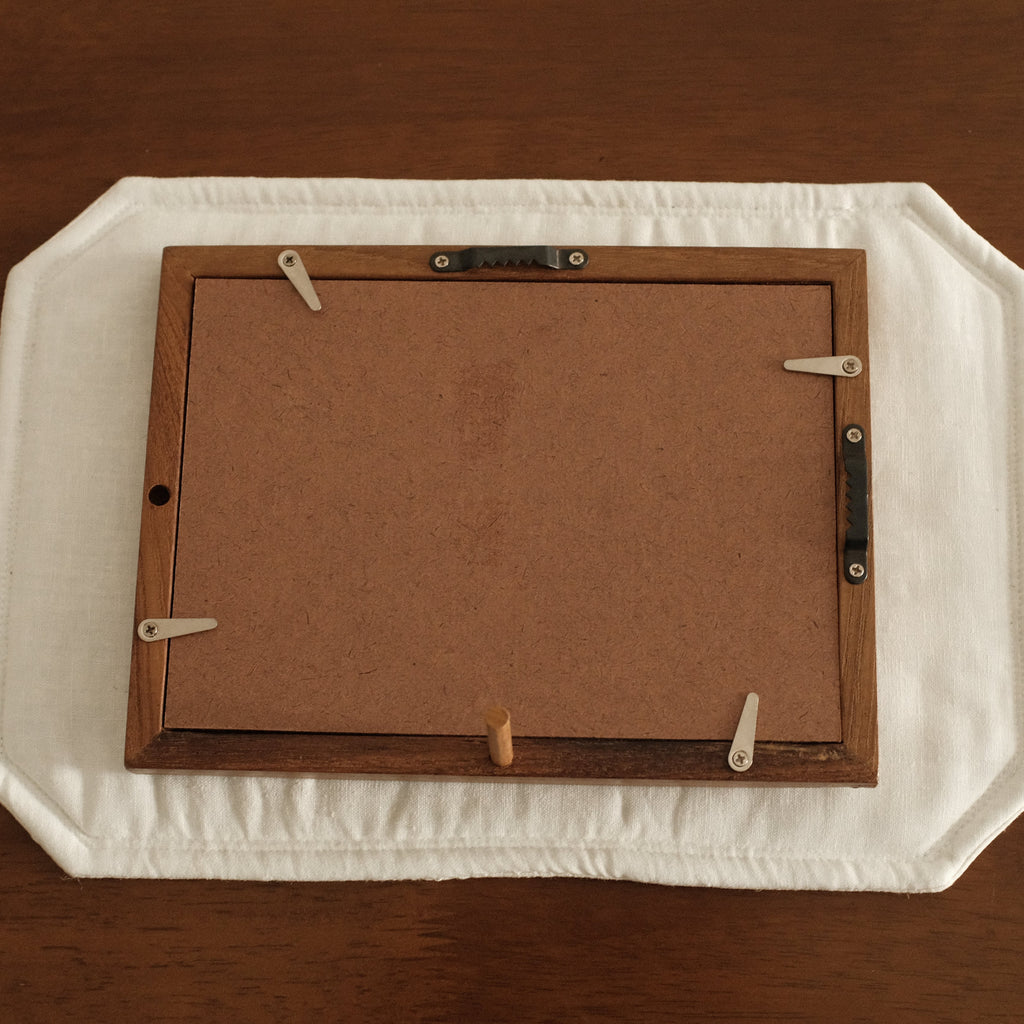 Backside of Teak wood frame on a white placemat with a wooden surface underneath