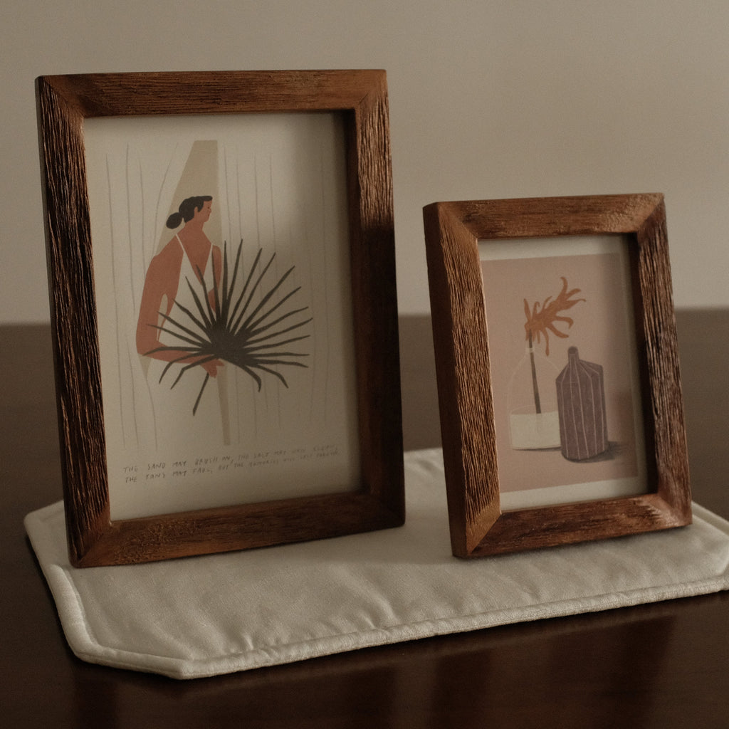 Two wooden-framed prints on a textured surface with a neutral background