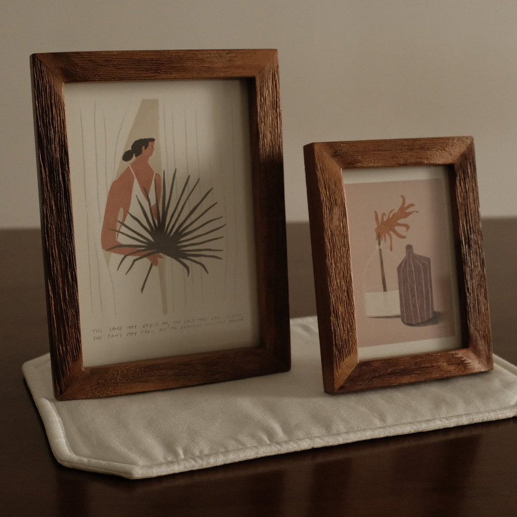 Two wooden-framed prints on a textured surface with a neutral background