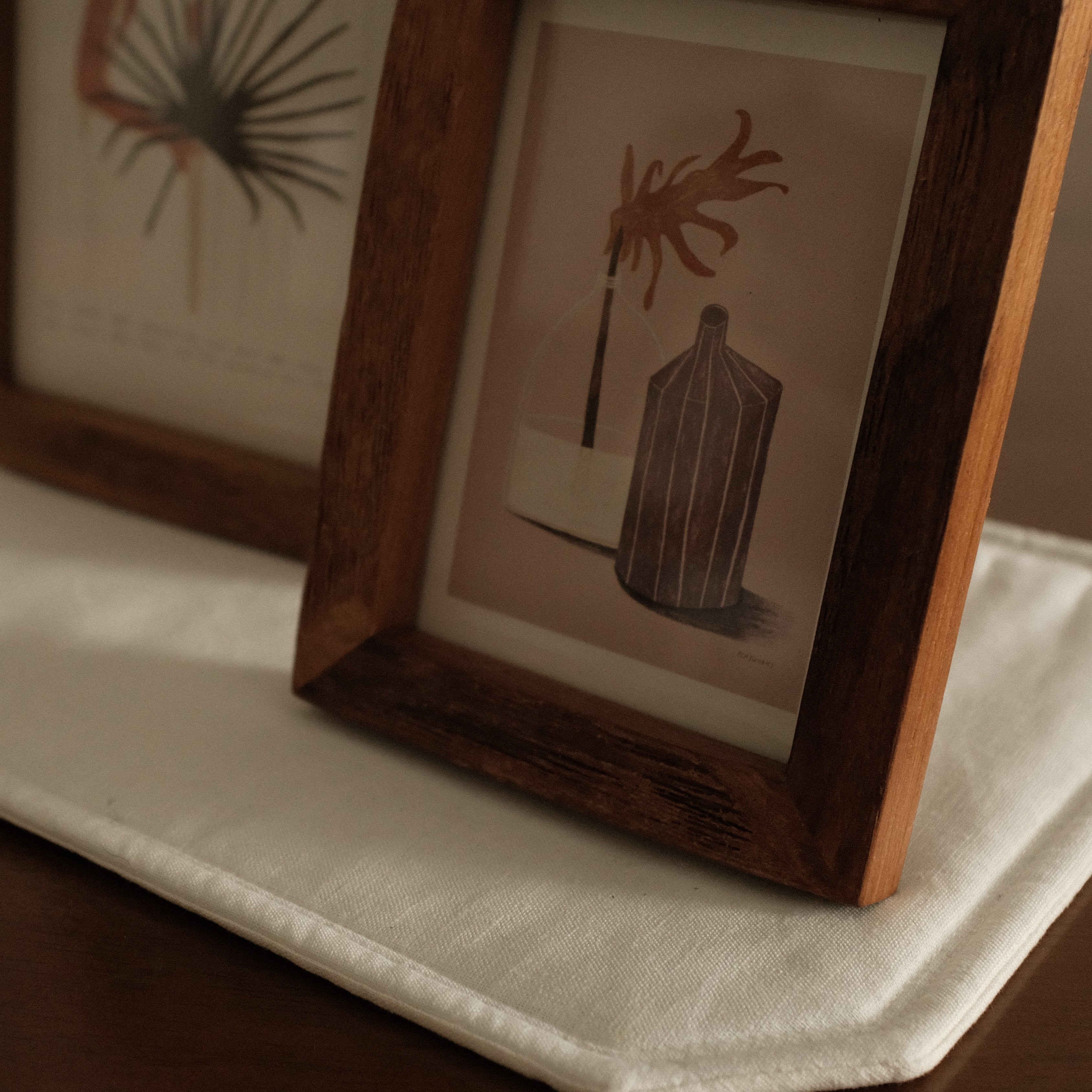 Two framed artworks on a white stand with a brown background