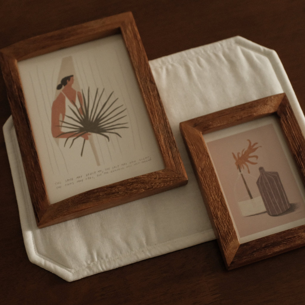 Two wooden-framed artworks on a white surface with a dark brown background