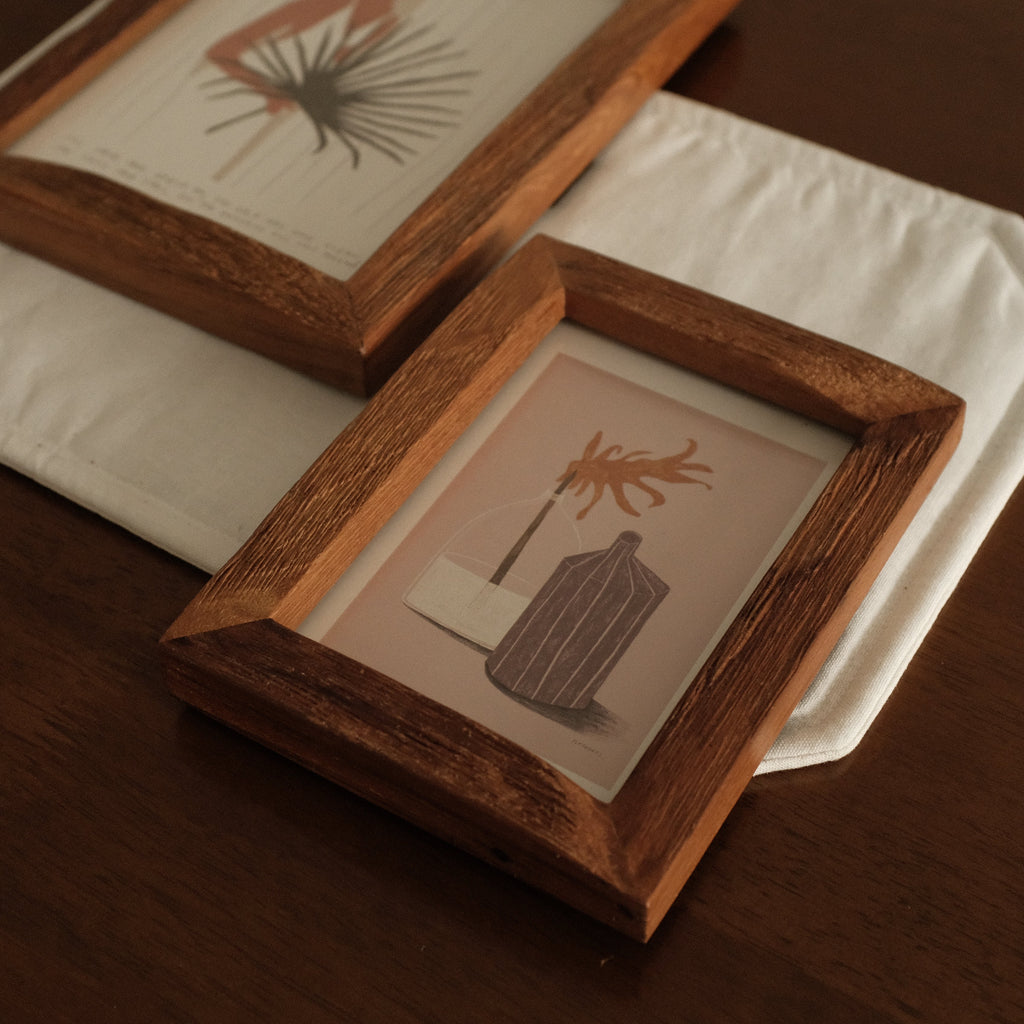 Two wooden picture frames with prints of plants on a white surface.