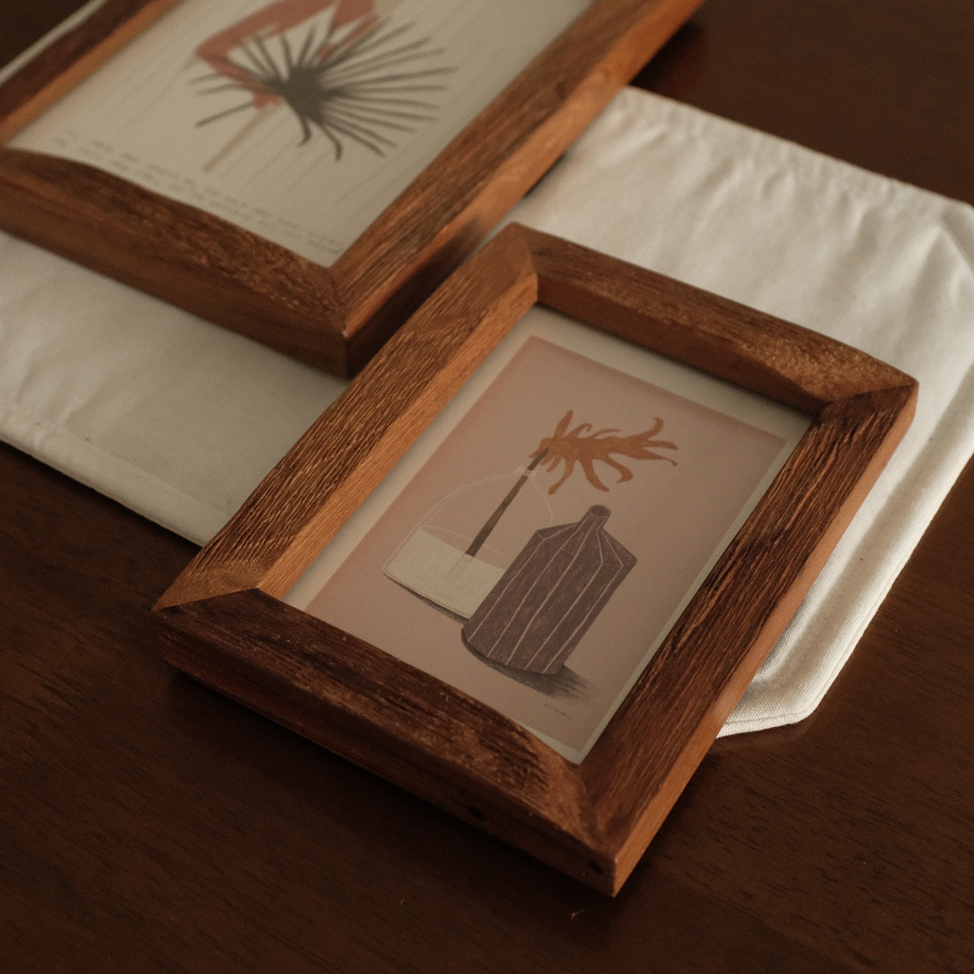 Two wooden picture frames with prints of plants on a white surface.