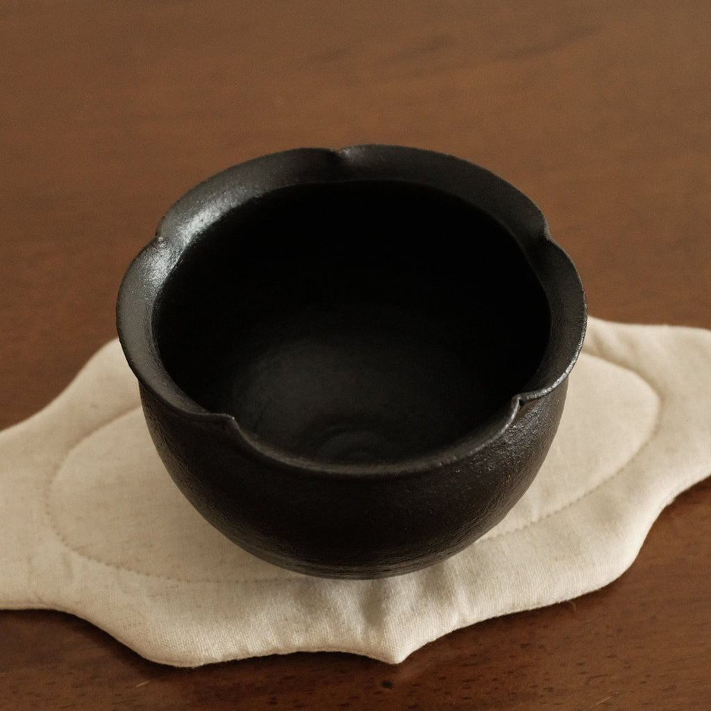 Black ceramic cup on a beige coaster with a brown background