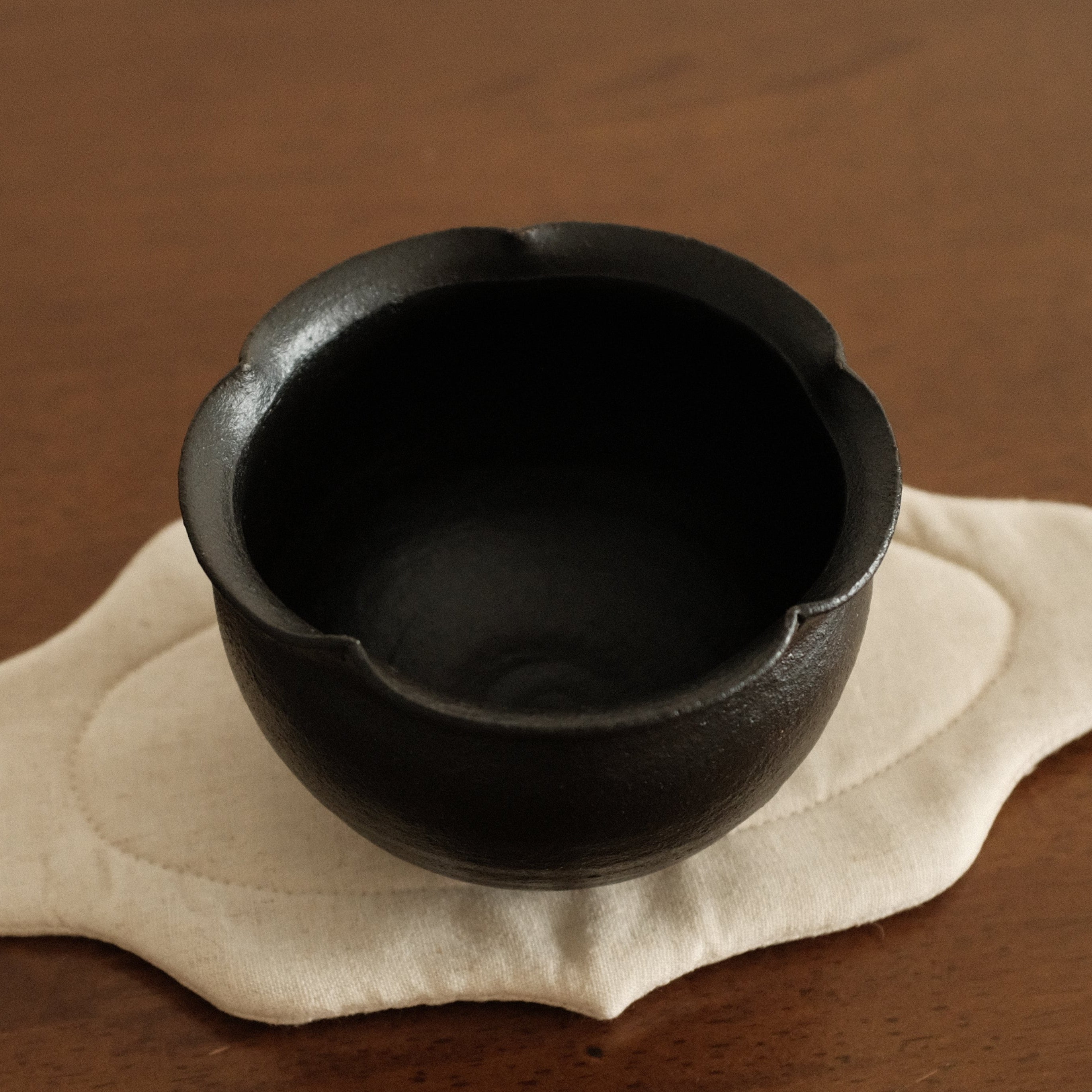 Black ceramic cup on a beige coaster with a brown background