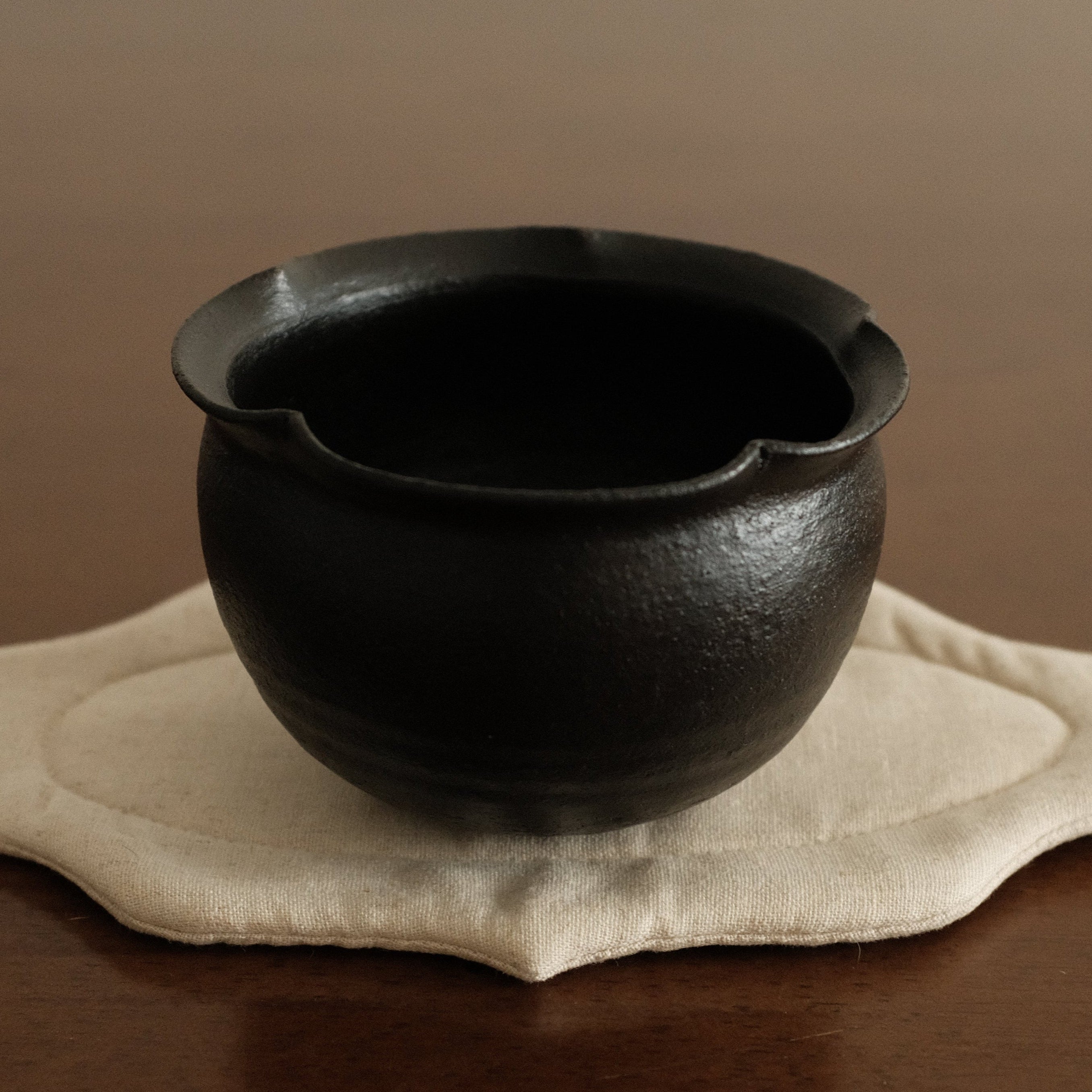 Black ceramic cup on a beige coaster with a brown background