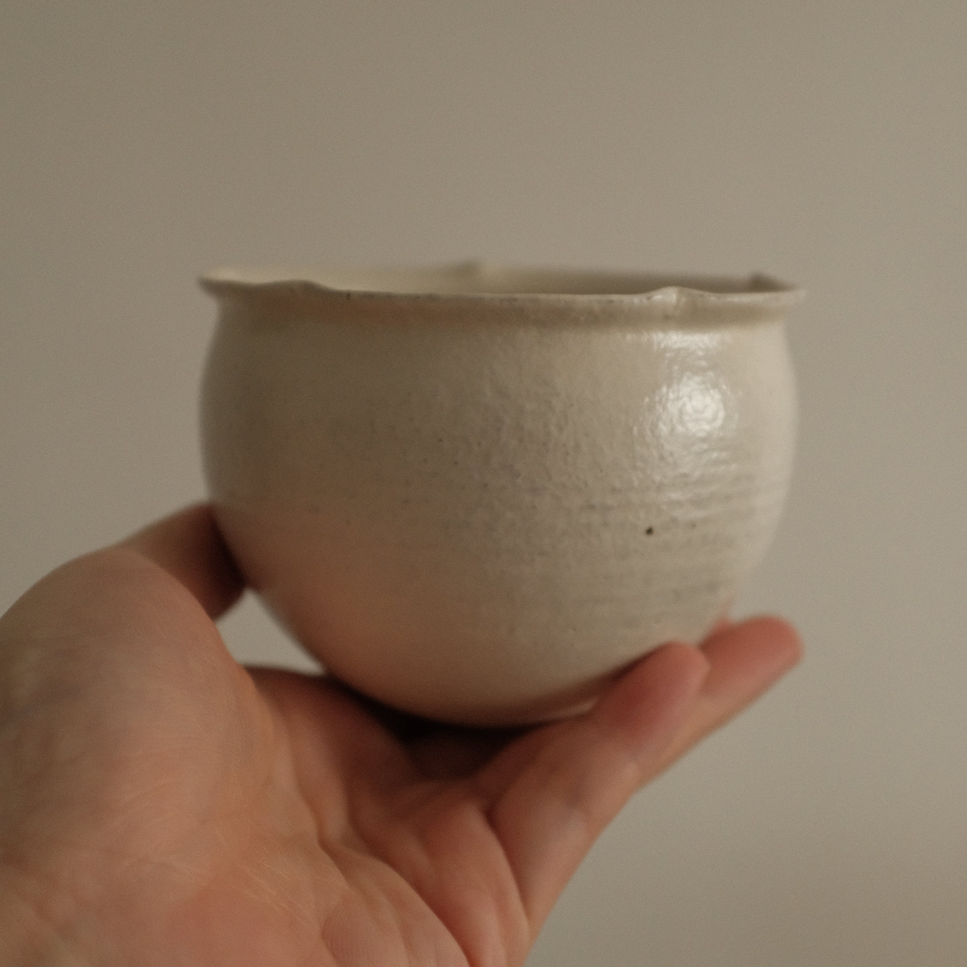 Hand holding a small ceramic floral rim cup against a plain background