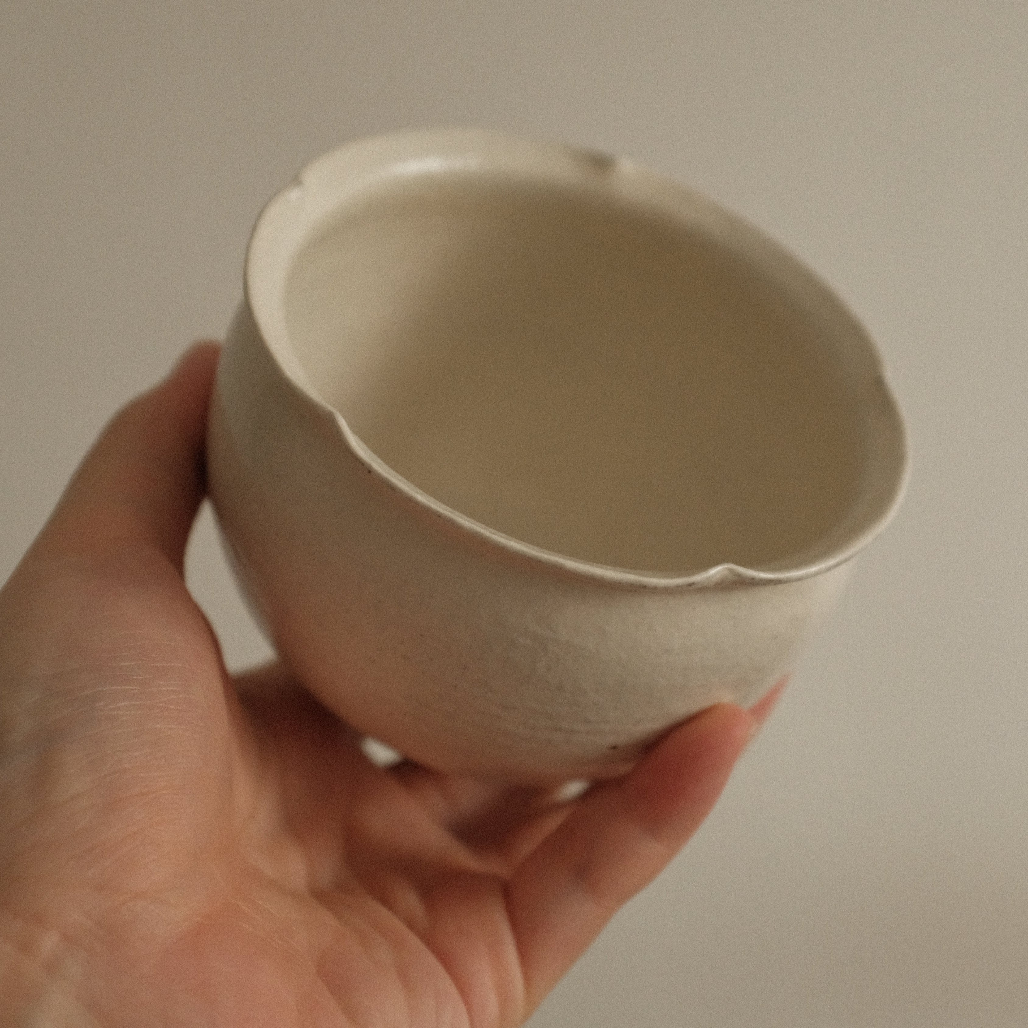 Hand holding a small ceramic floral rim cup against a plain background