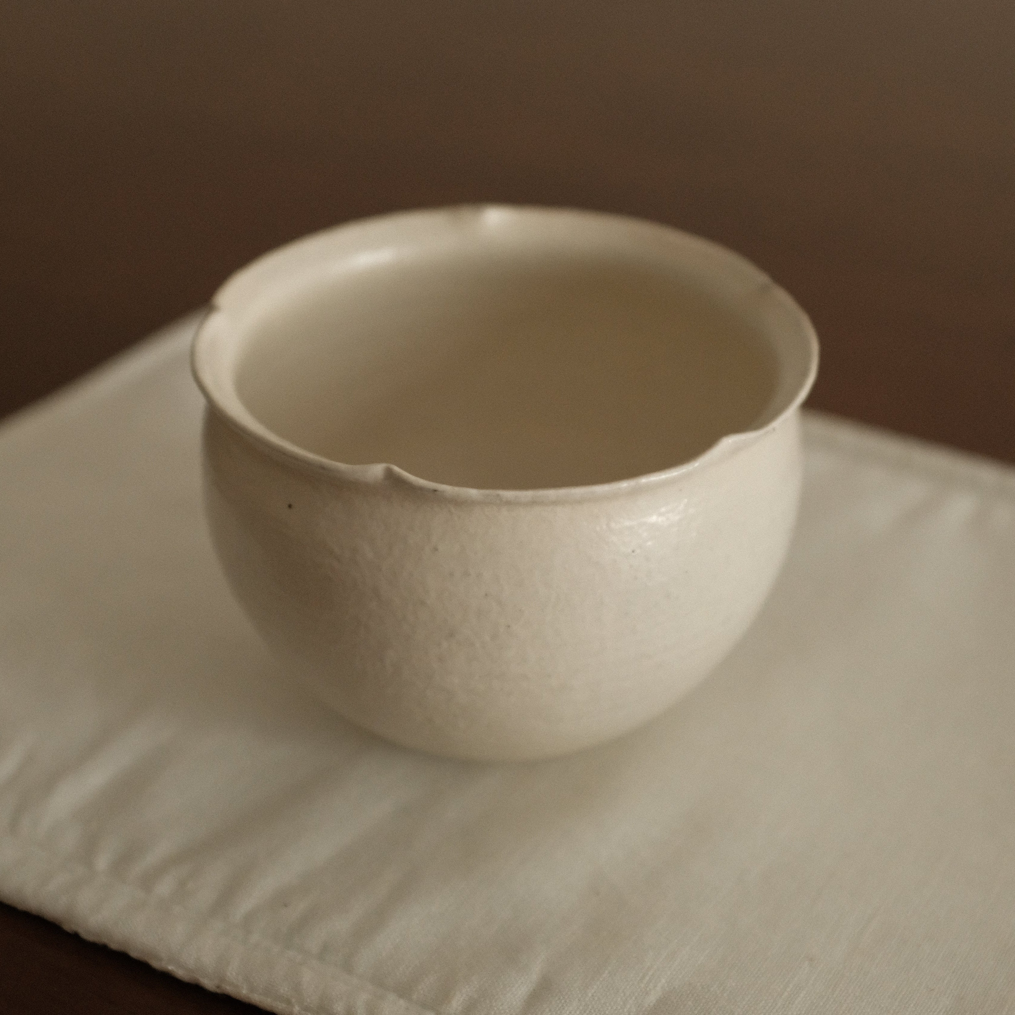 White ceramic floral rim cup on a textured white surface with a brown background