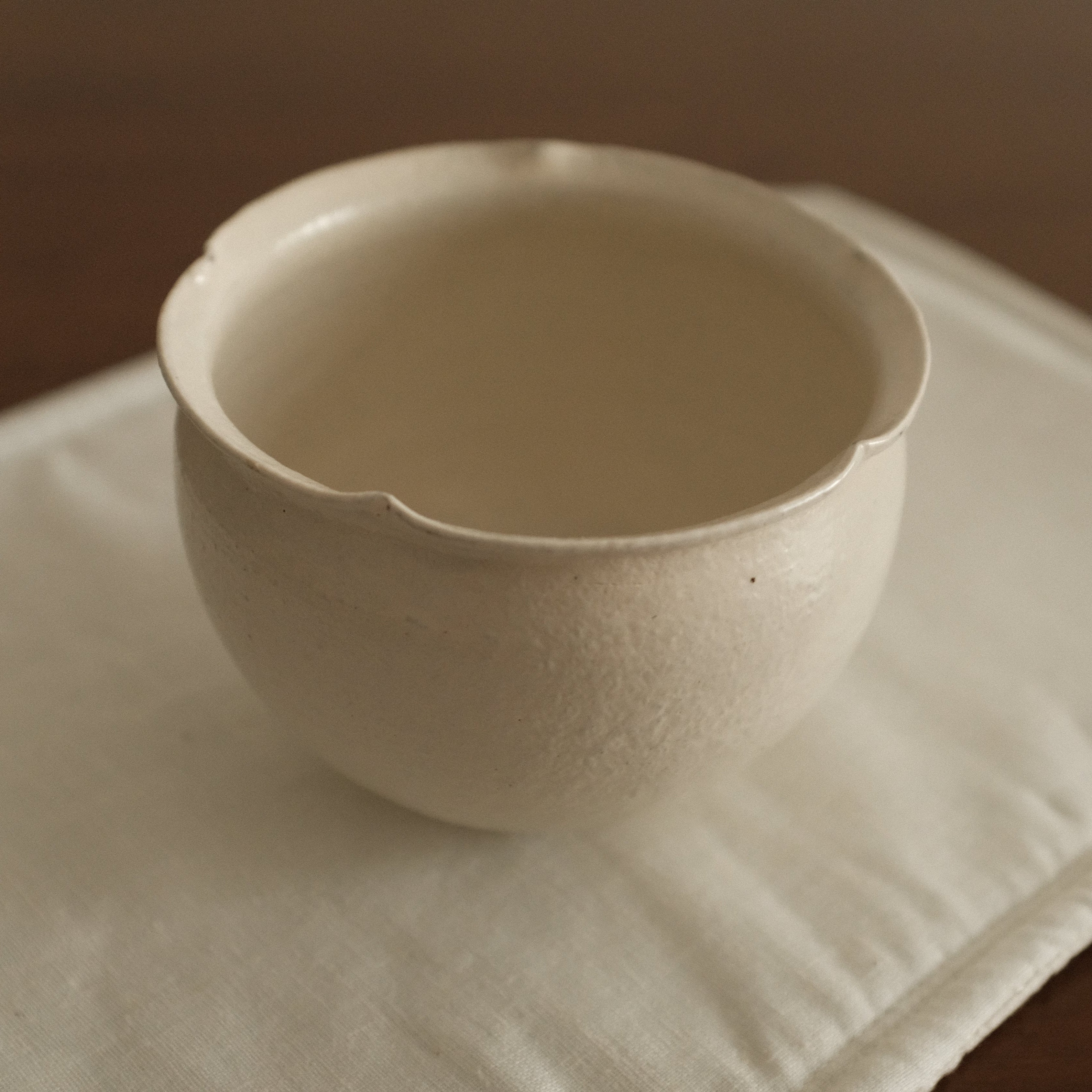 White ceramic floral rim cup on a textured white surface with a brown 
