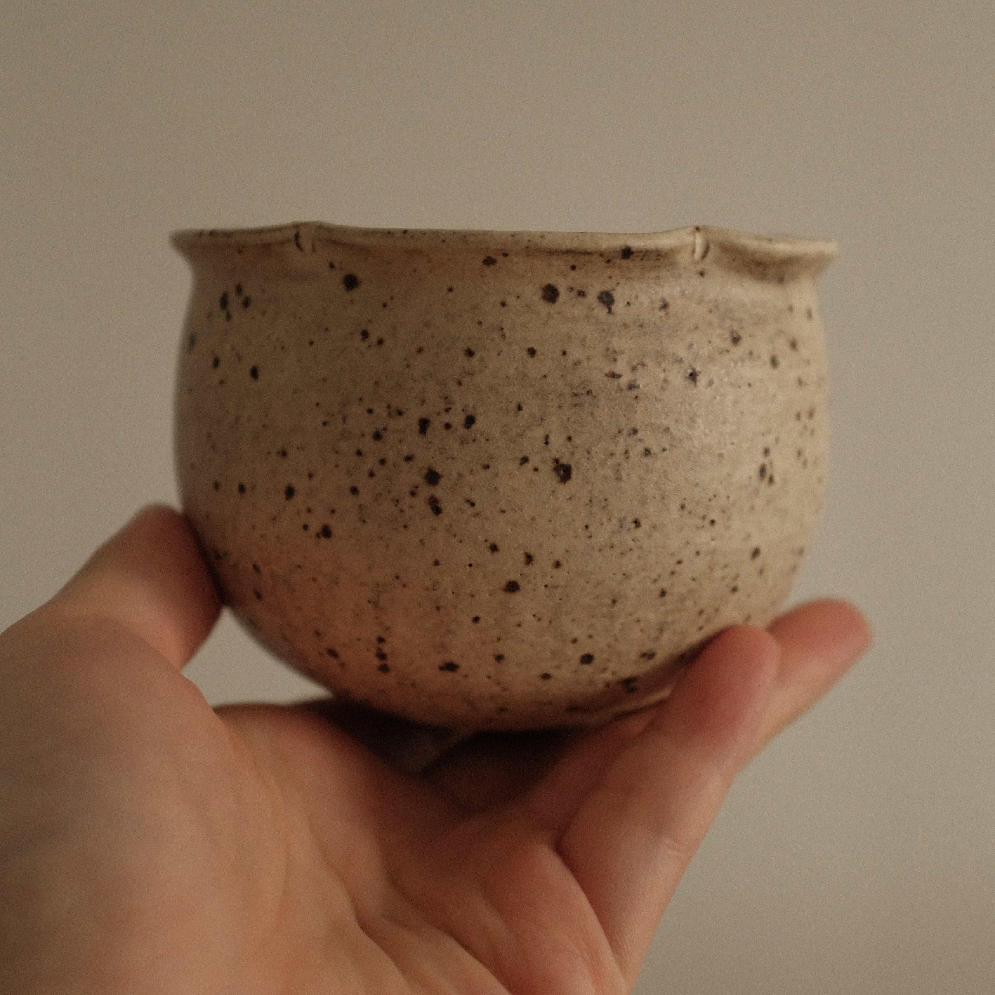 Hand holding a small speckled ceramic grey beige floral rim cup against a plain background