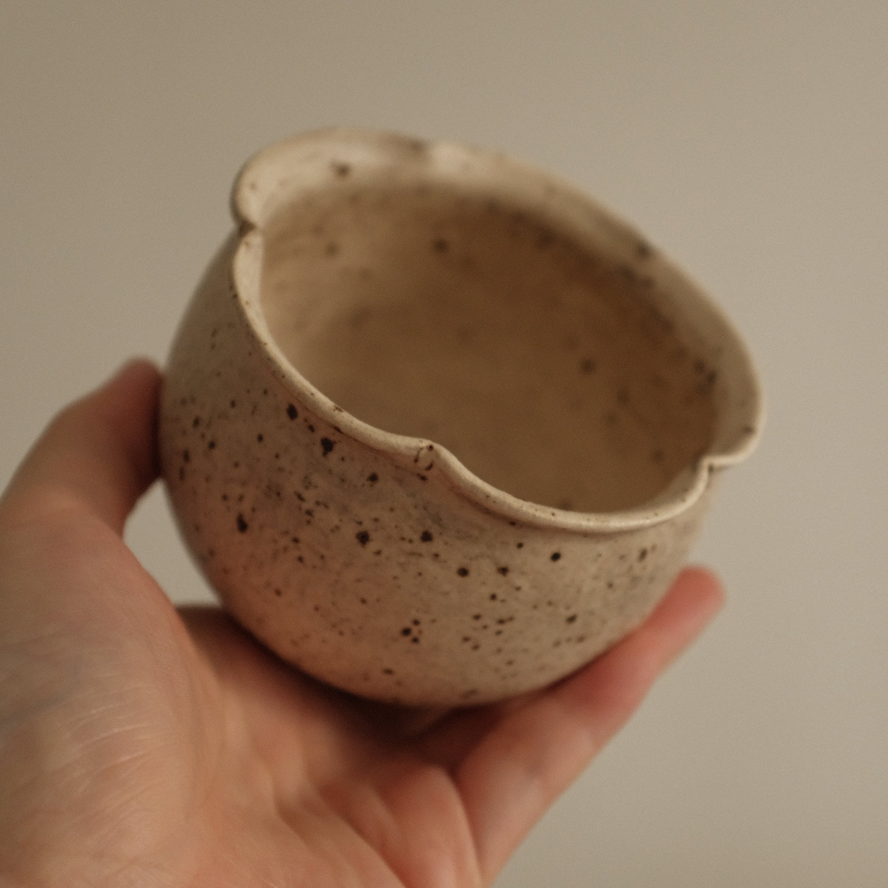 Hand holding a small speckled ceramic grey beige floral rim cup against a plain background