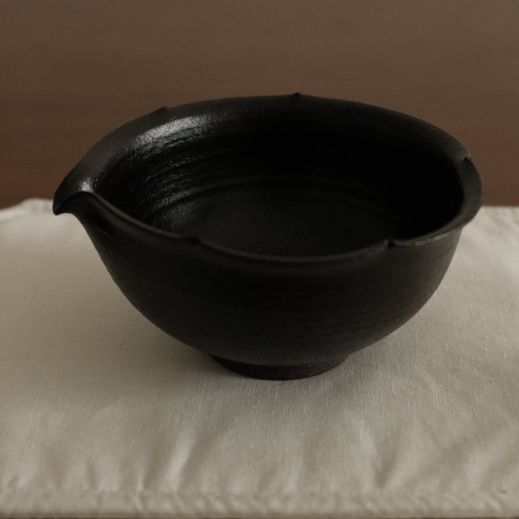 Black ceramic floral rim chawan matcha bowl on a white square cloth with a brown background