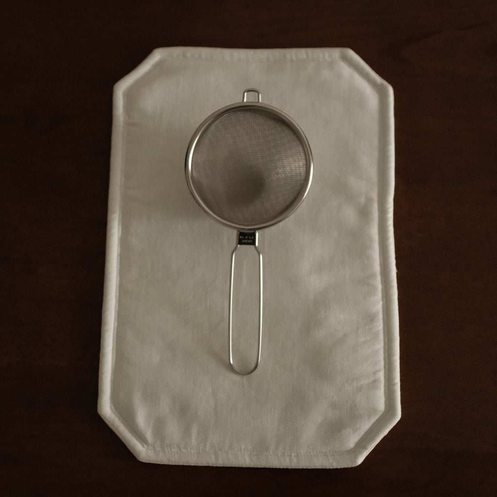 Metal strainer on a folded white cloth against a dark background