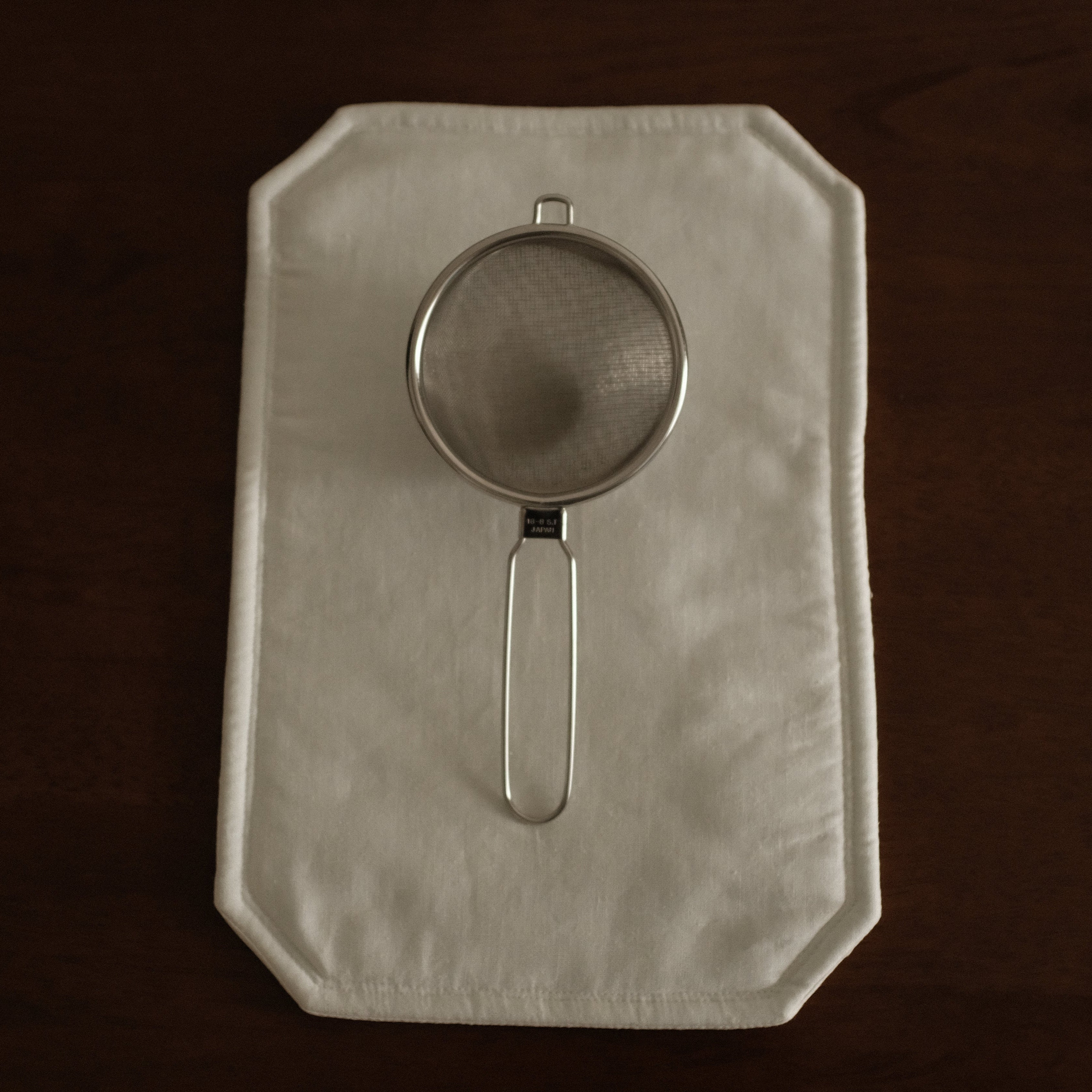Metal strainer on a folded white cloth against a dark background
