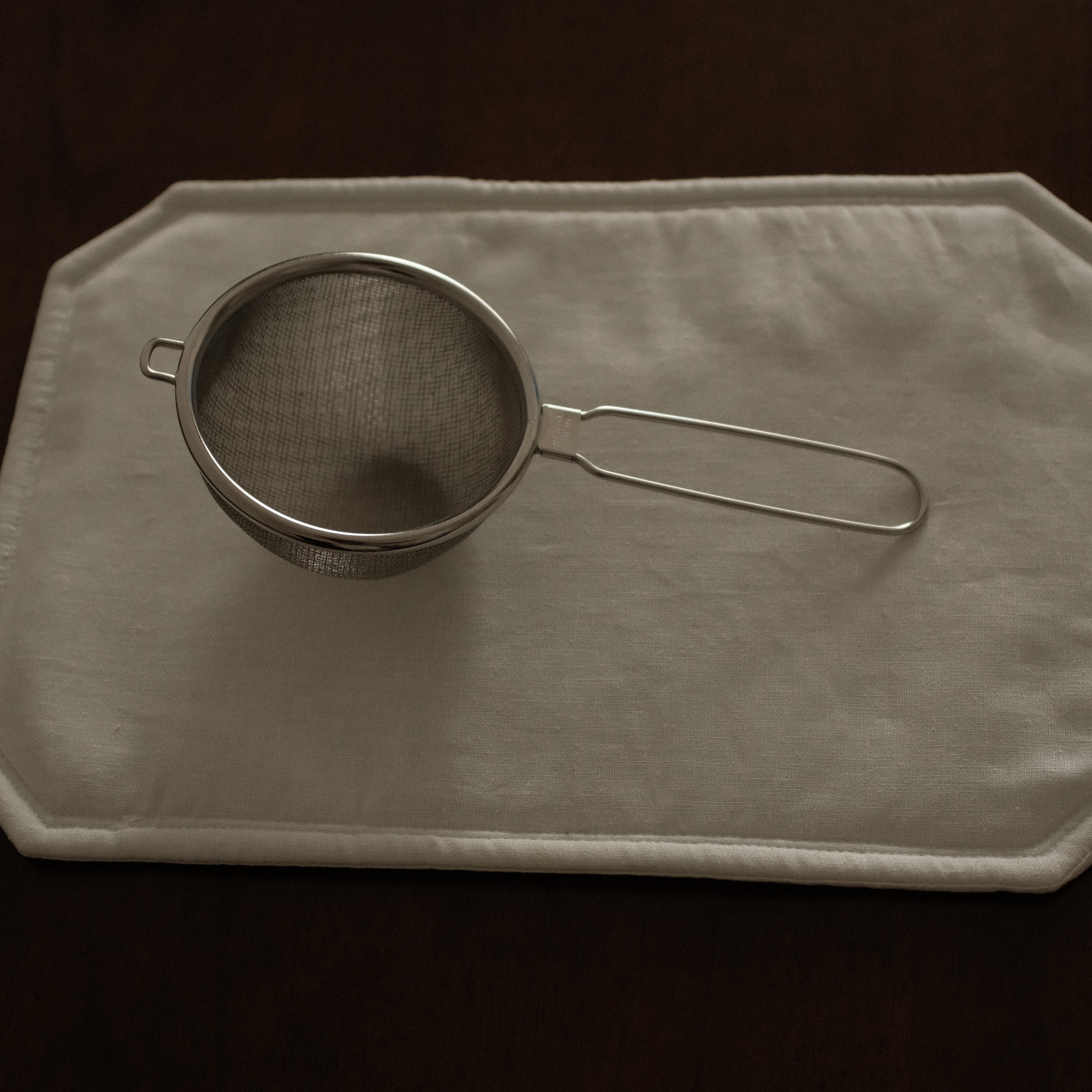Metal strainer on a beige cloth with a dark background