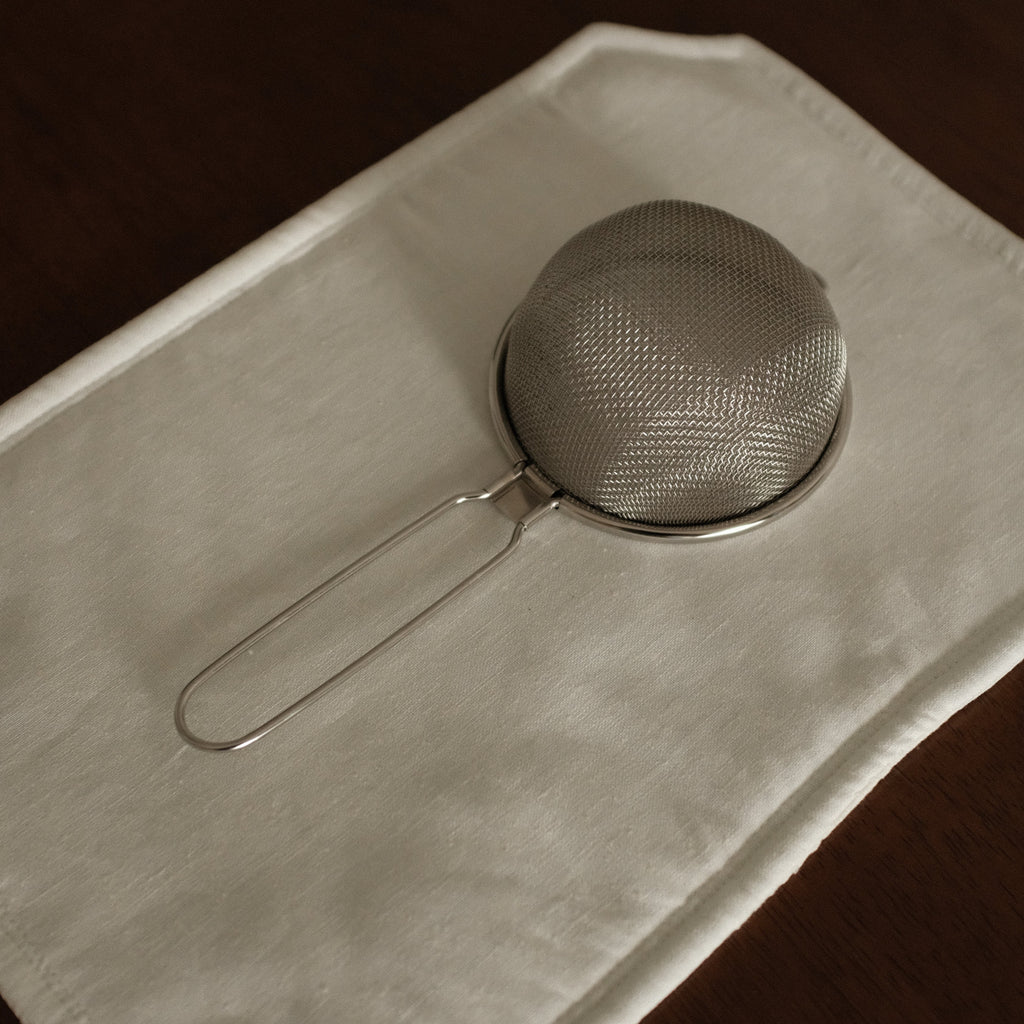 Metal strainer on a folded white cloth against a dark background