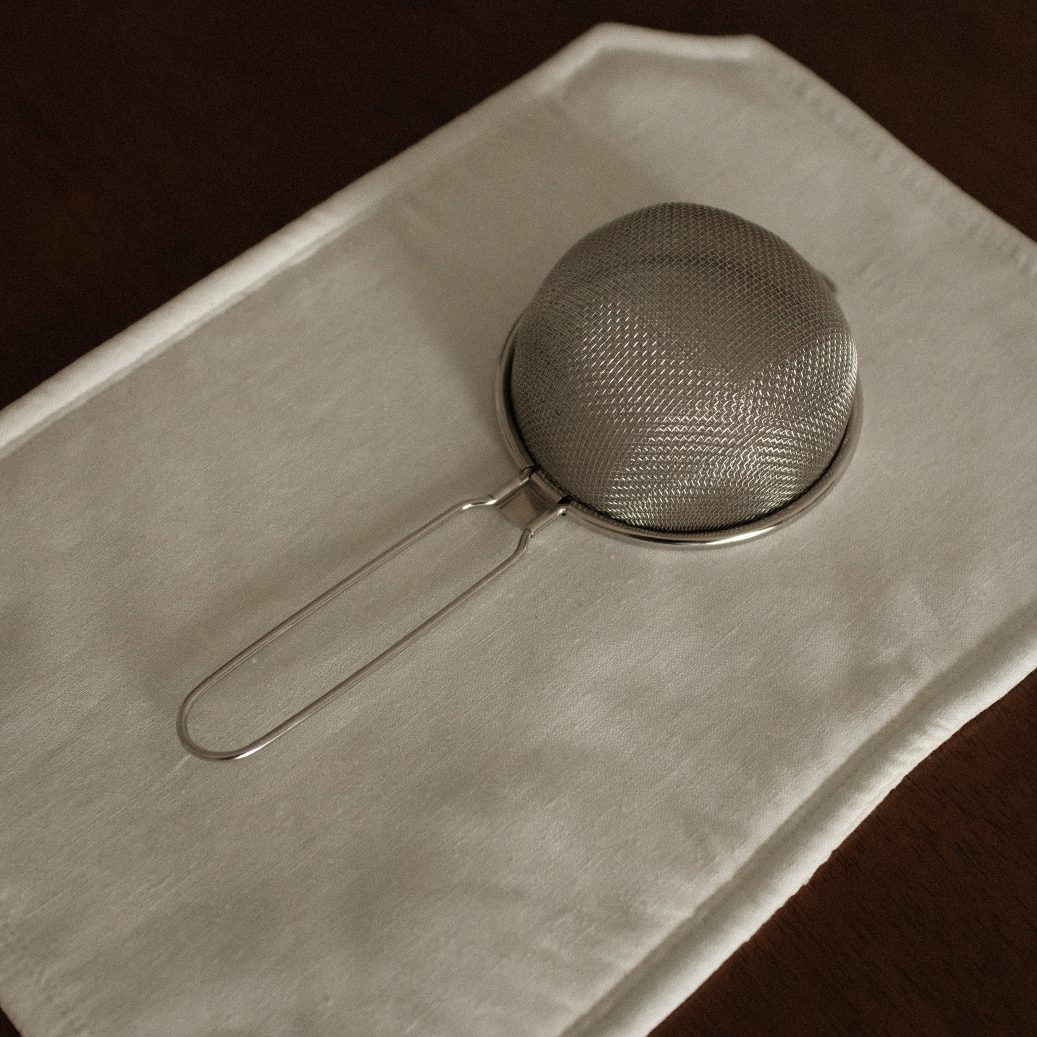Metal strainer on a folded white cloth against a dark background