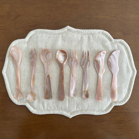 Set of mother of pearl cutlery on a decorative placemat with a wooden background