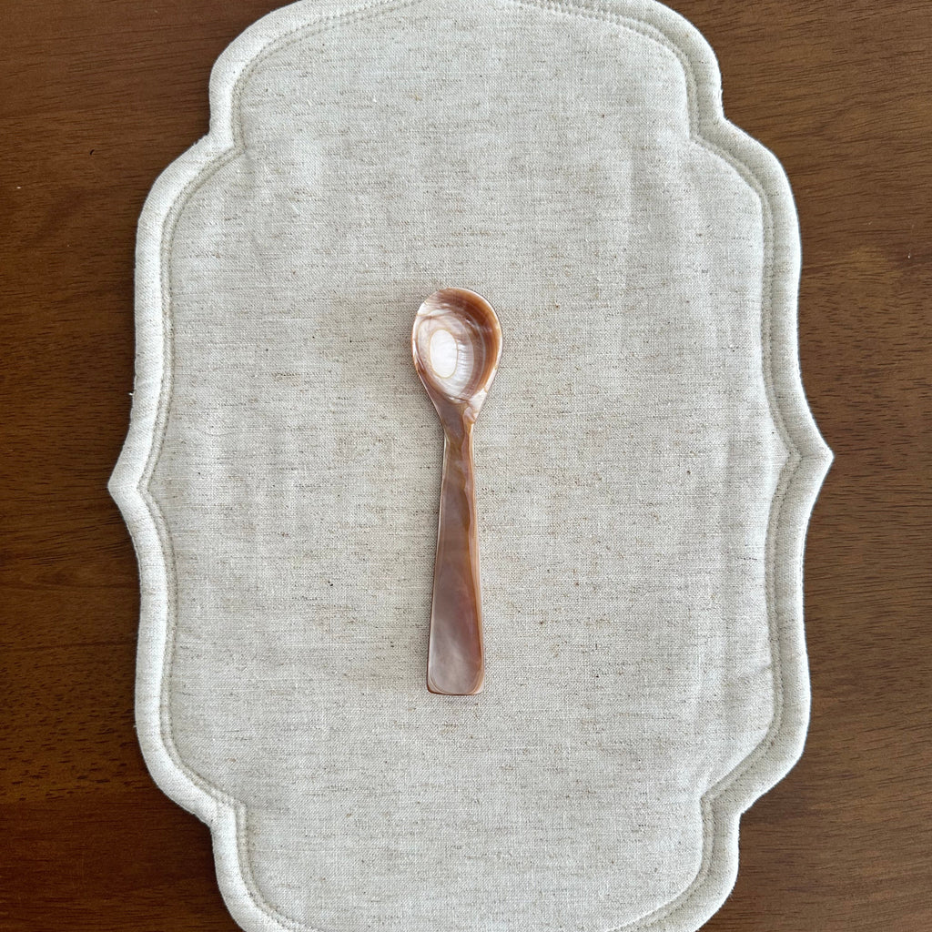 Decorative white placemat with a small decorative spoon on a wooden surface