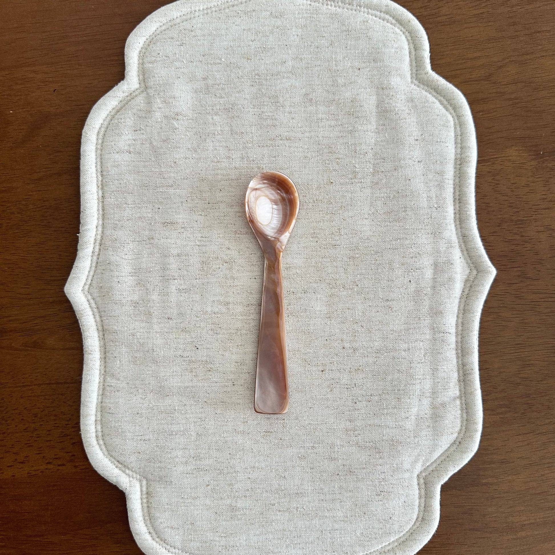 Decorative white placemat with a small decorative spoon on a wooden surface