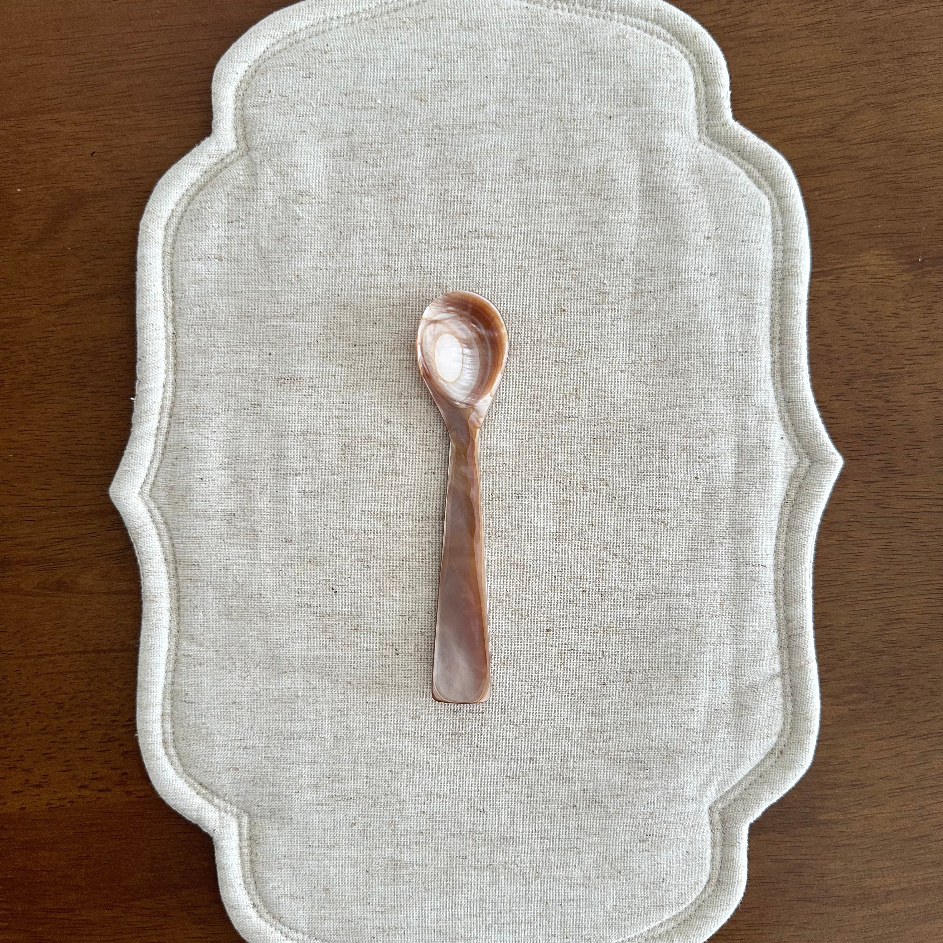 Decorative white placemat with a small decorative spoon on a wooden surface