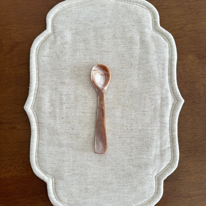 Decorative white placemat with a small decorative spoon on a wooden surface