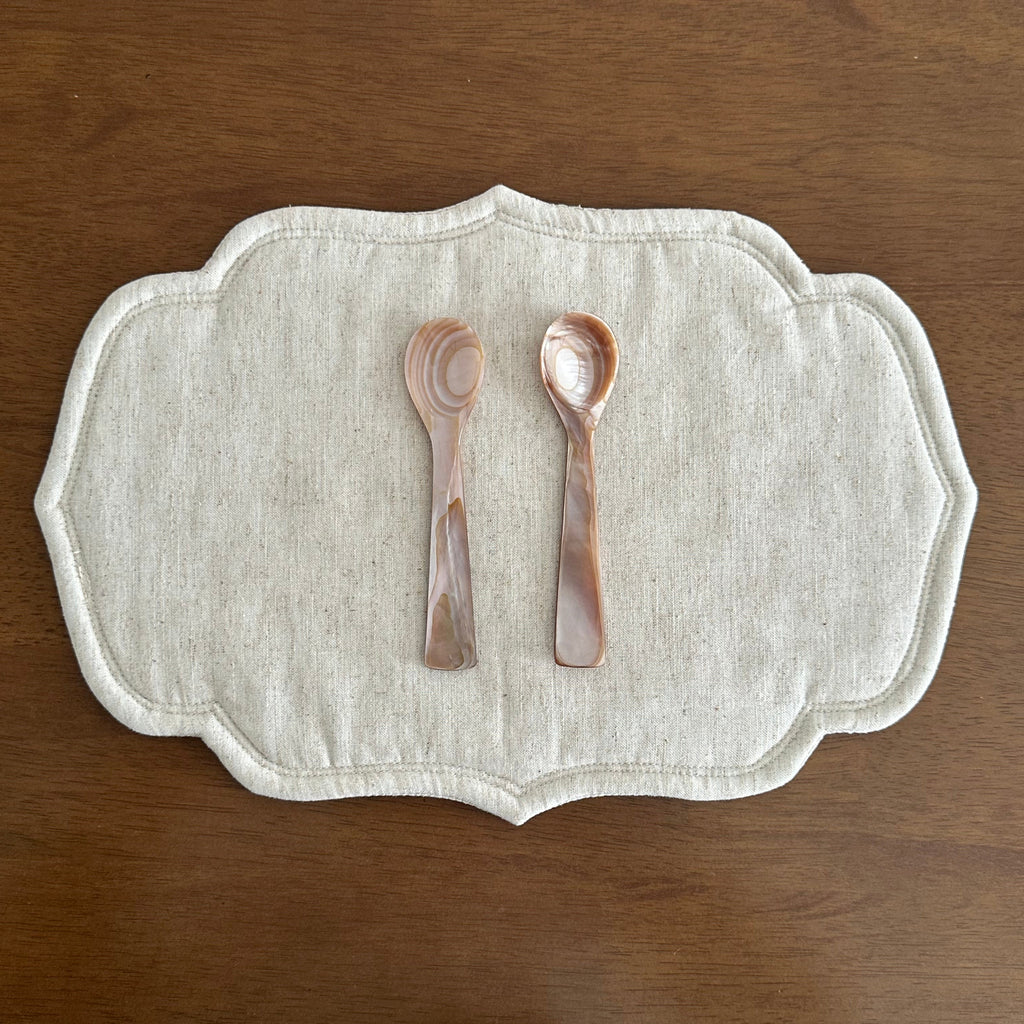 Decorative white mat with two pink spoons on a wooden surface