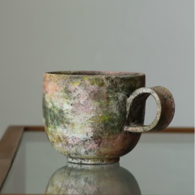 Vintage ceramic mug with a textured surface on a reflective surface.