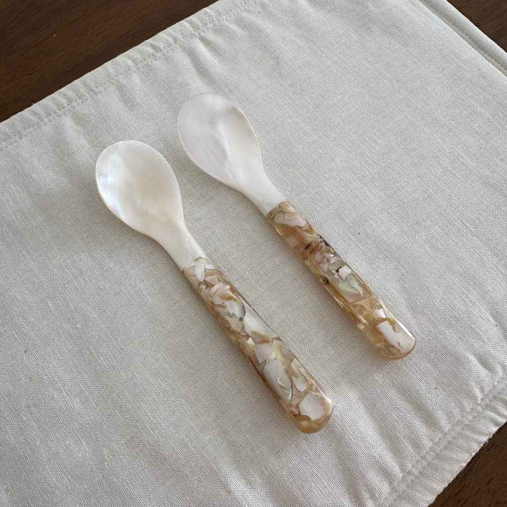 Four decorative seashell spoons on a white cloth with a wooden background