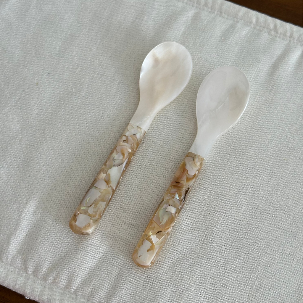 Four decorative seashell spoons on a white cloth with a wooden background
