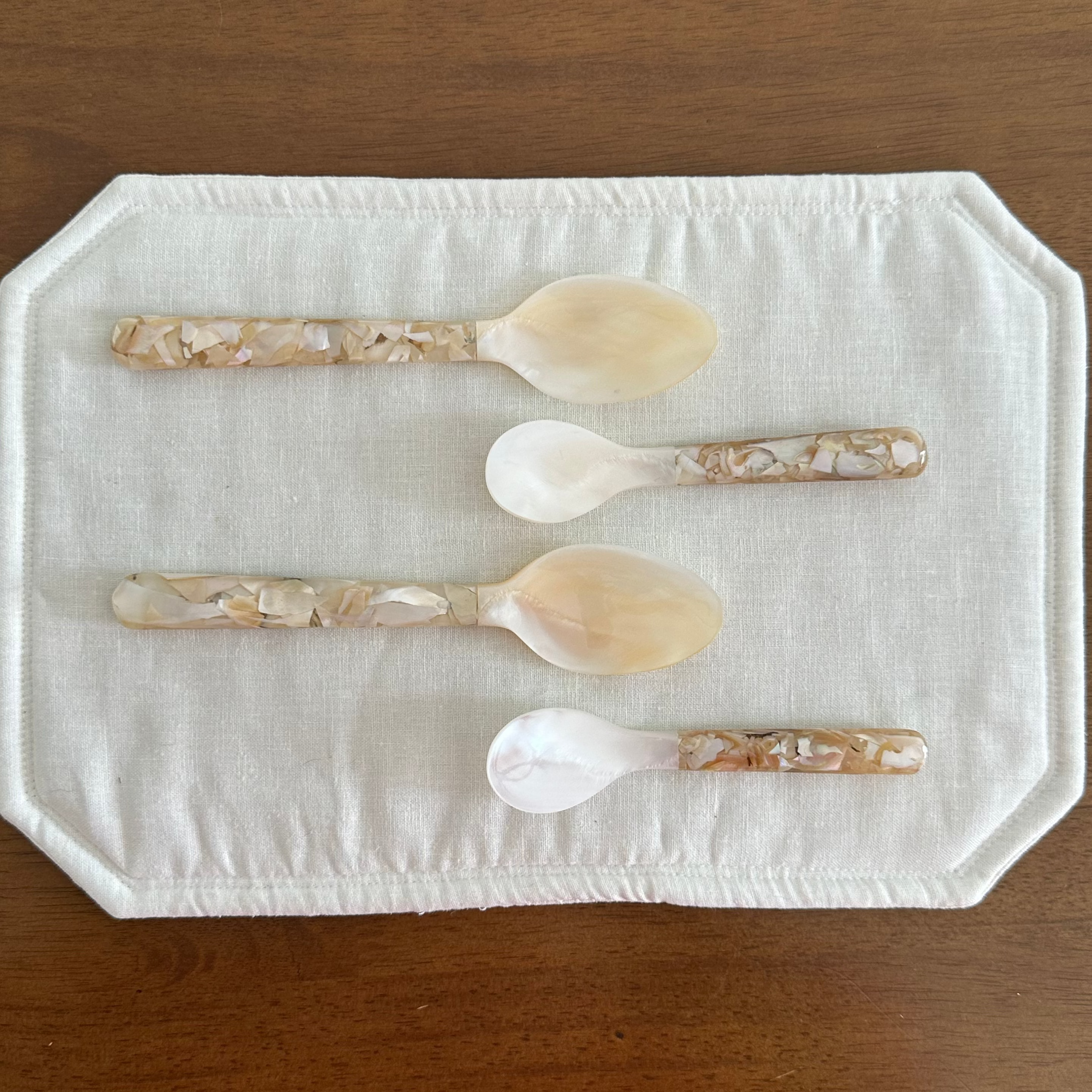 Four decorative seashell spoons on a white cloth with a wooden background
