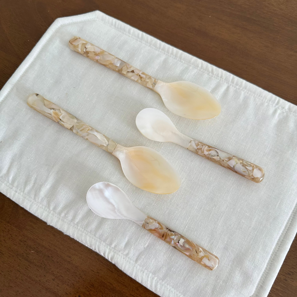 Four decorative seashell spoons on a white cloth with a wooden background