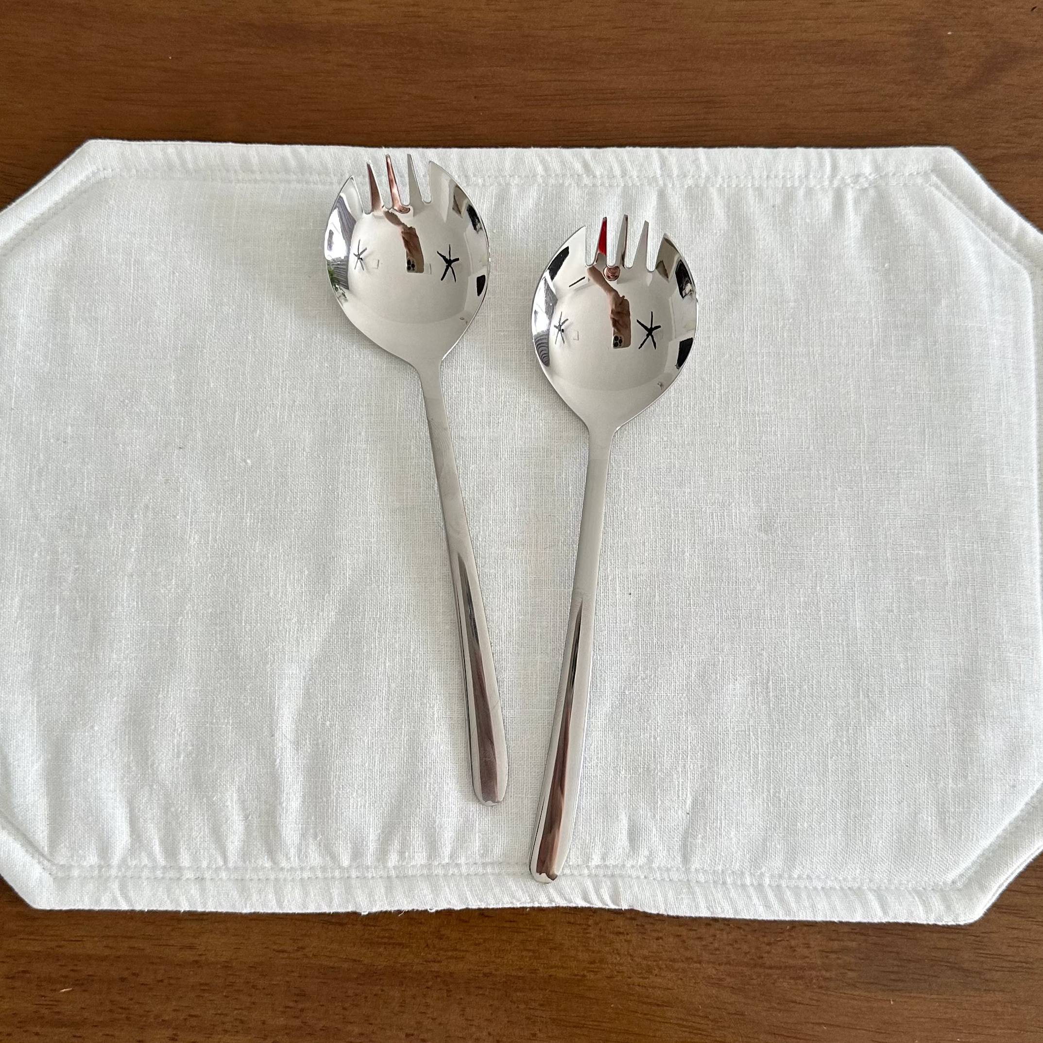 Silver salad servers on a white placemat with a wooden background