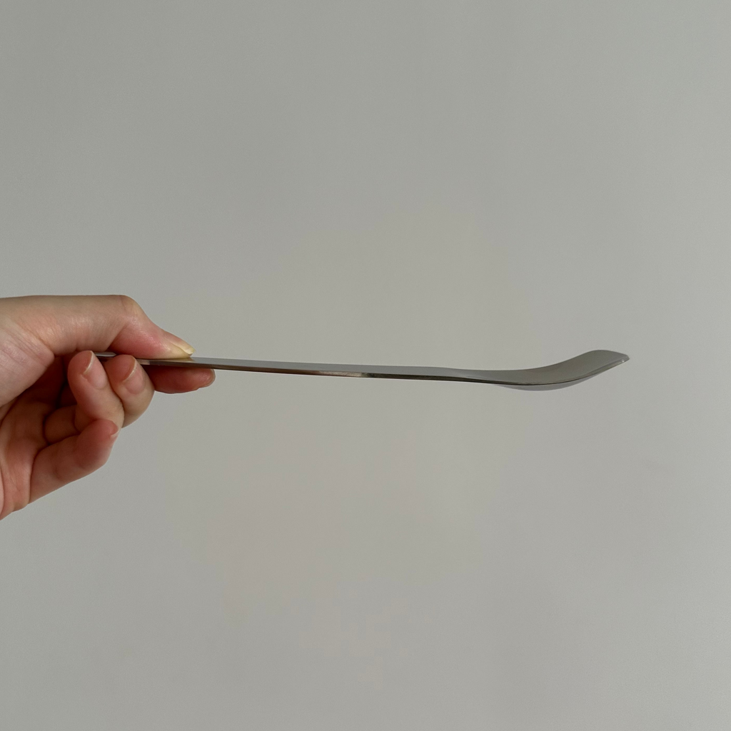 Hand holding a silver spoon against a plain background