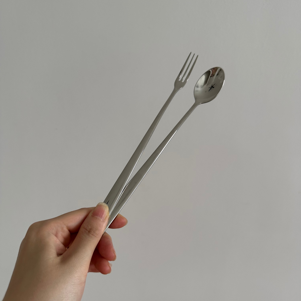 Hand holding a silver fork and spoon against a plain background