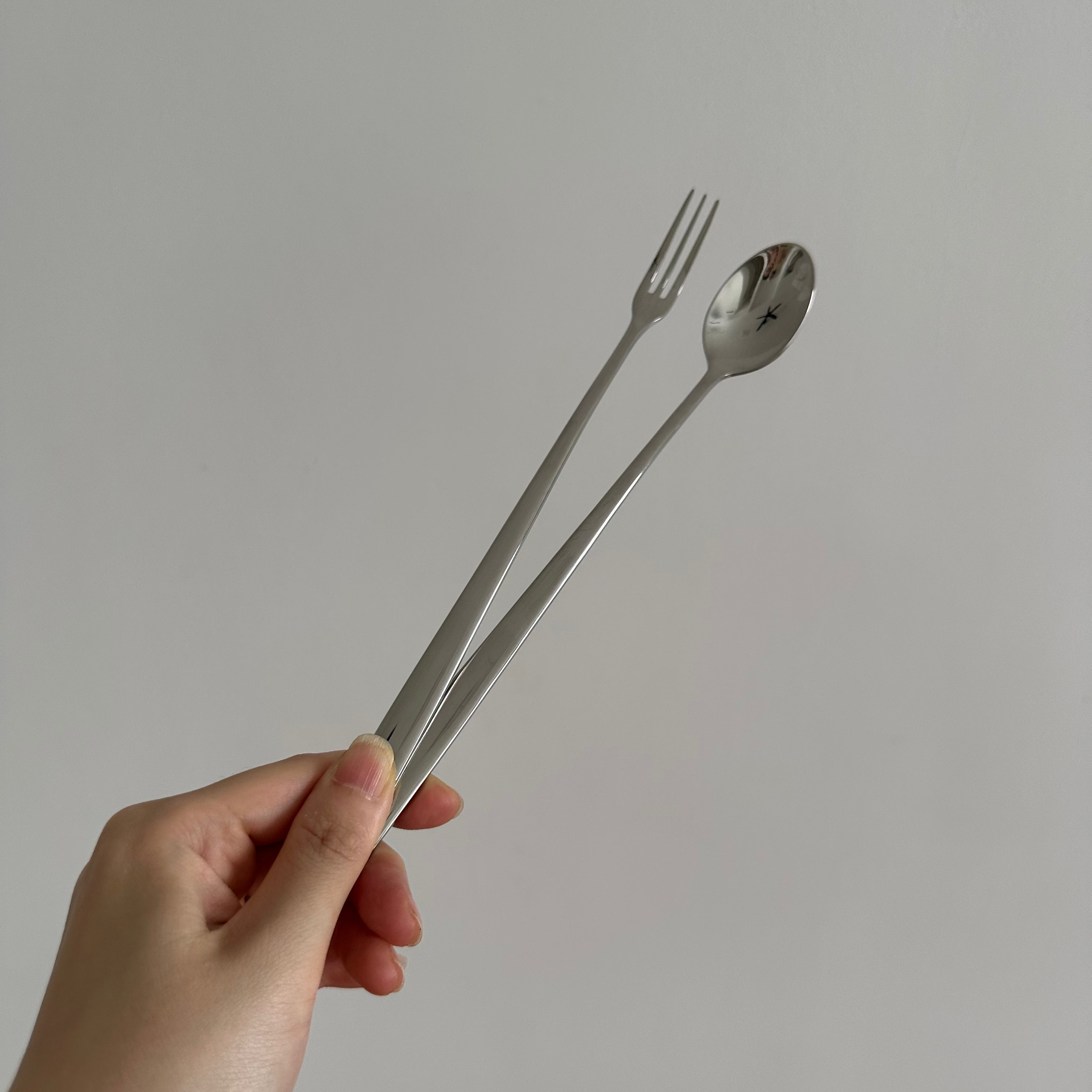 Hand holding a silver fork and spoon against a plain background
