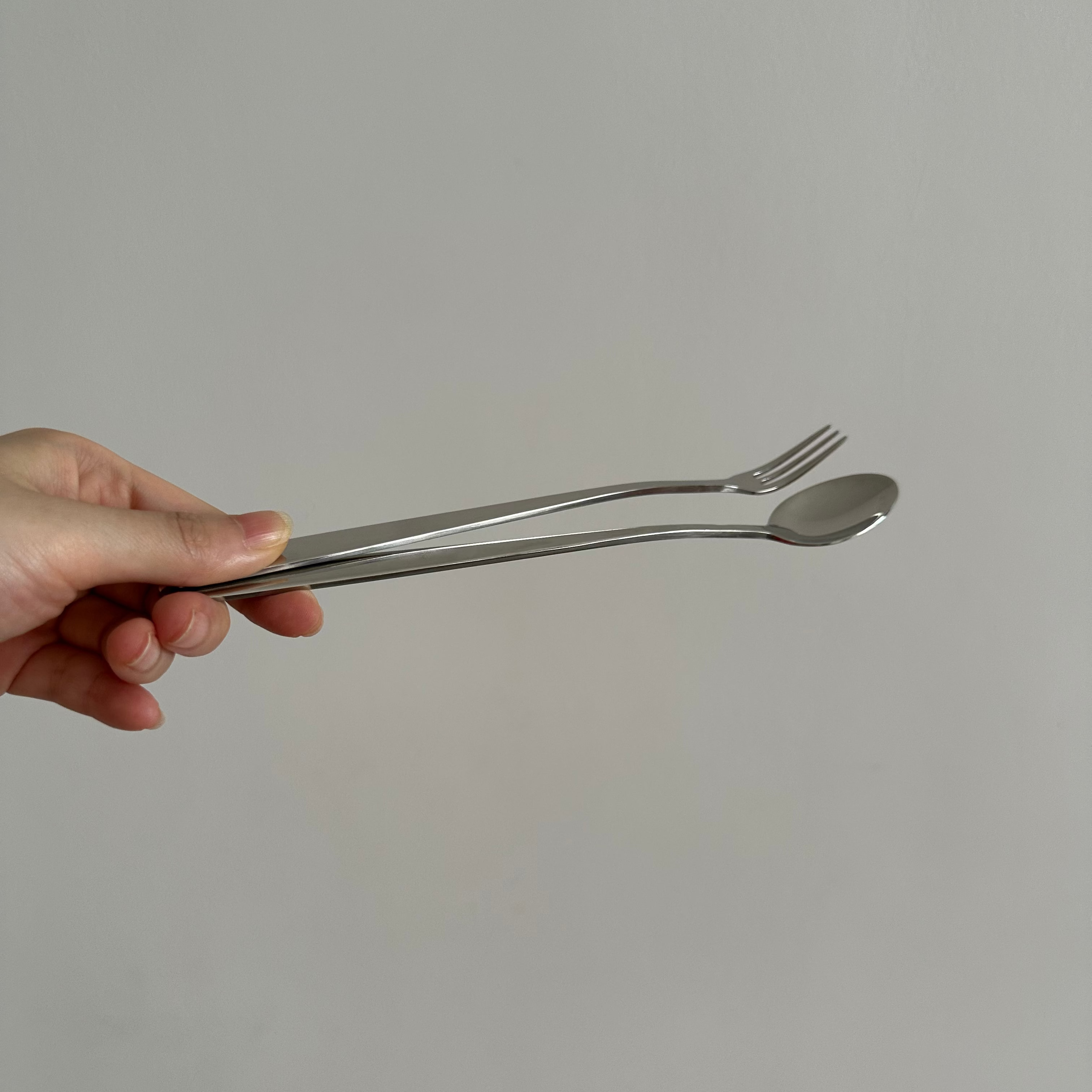 Hand holding a silver fork and spoon against a plain background