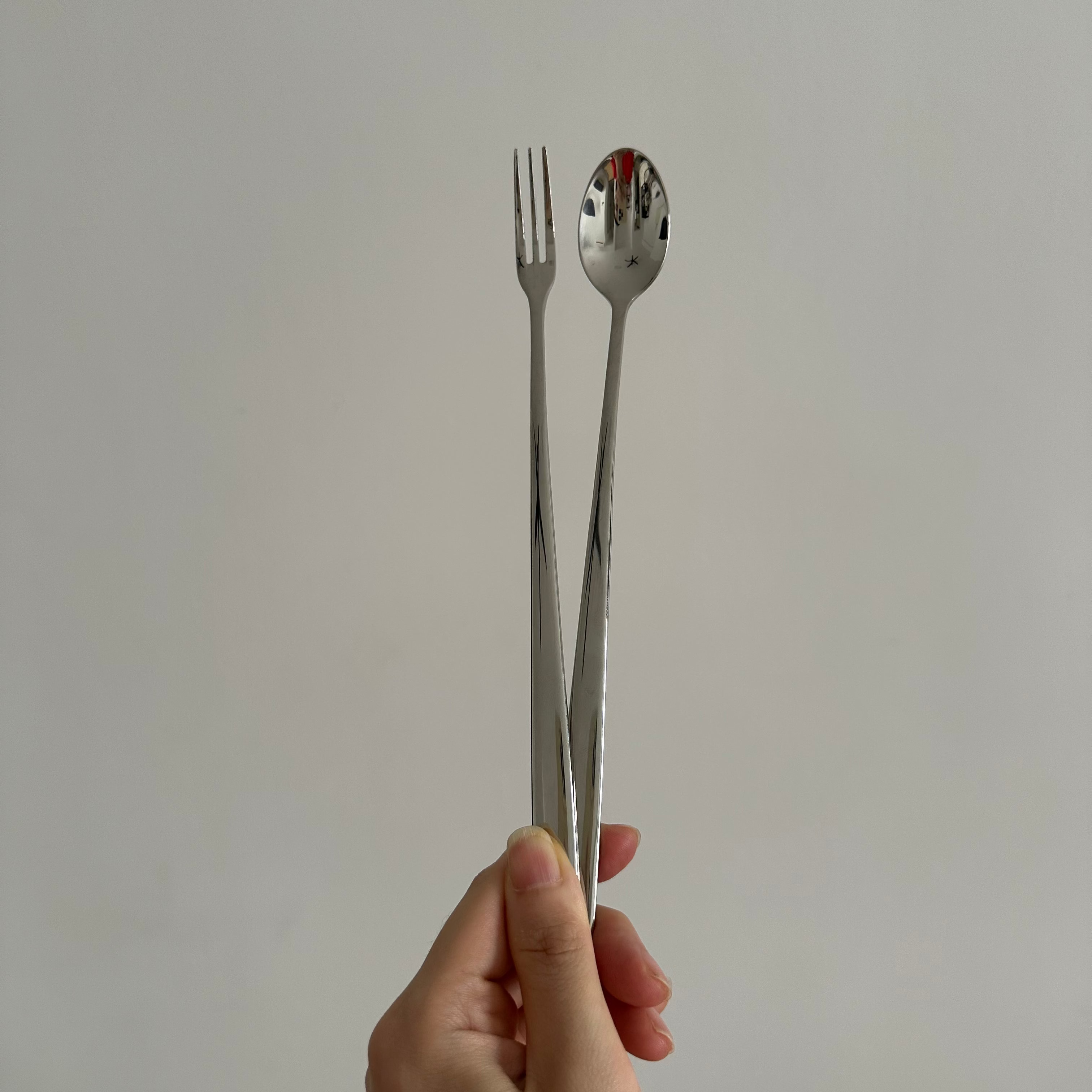 Hand holding a silver fork and spoon against a plain background