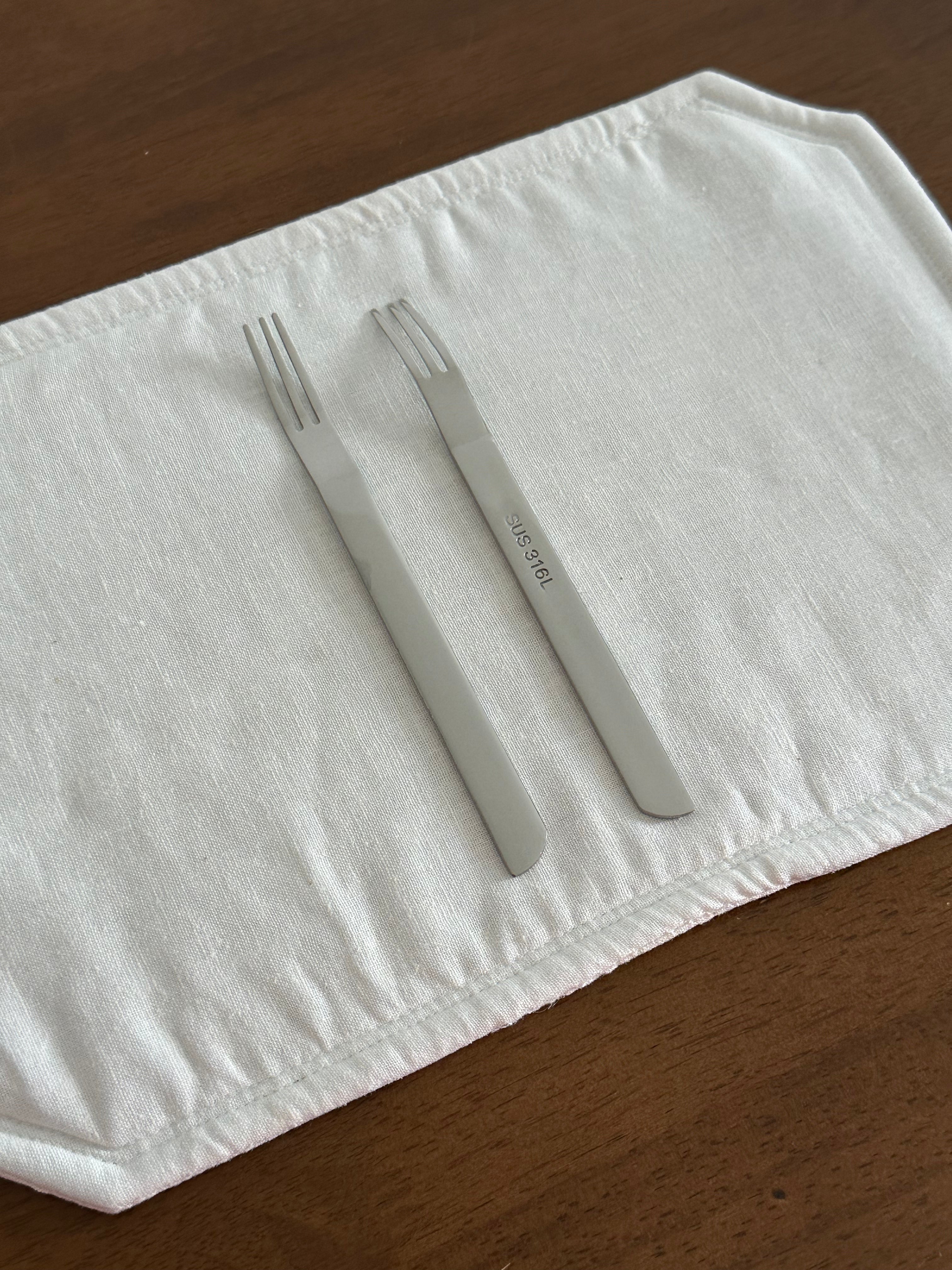 Two silver forks on a white cloth with sus 316L on a wooden surface.