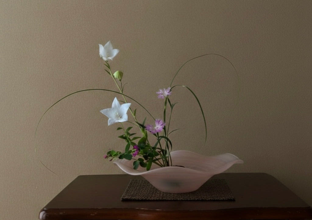 Floral arrangement in a pink bowl on a wooden table against a plain wall.