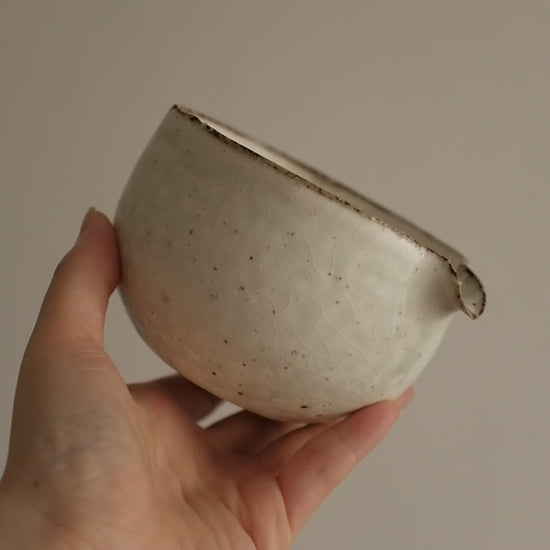Handcrafted by artisan Yu Ming Li, this katakuchi matcha bowl embodies the harmony of tradition and subtle artistry. Its distinctive spouted form—designed for whisking and gracefully pouring matcha—also makes it a versatile piece for serving sauces, dressings, or shared tea moments.

Finished in a soft matte white powdered glaze, the surface carries gentle green undertones that emerge like mist over porcelain hills, shifting beautifully with light and shadow. The glaze’s natural variations ensure that each 